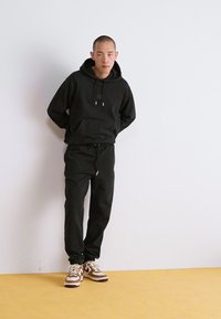 Sort hættetrøje med snøre og frontlomme, parret med matchende sorte sweatpants. Brun og hvid atletiksko. Minimalistisk design.