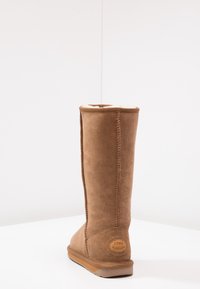 Bota de ante marrón hasta la rodilla con un suave forro interior, que presenta una punta redondeada y una suela de goma color beige. Logotipo de EMU Australia en el tacón.