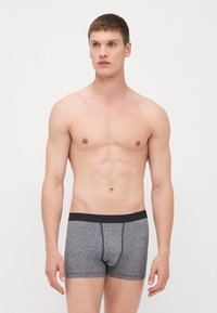 Männer graue Boxershorts mit einem schwarzen Bund. Hergestellt aus einem weichen, dehnbaren Stoff mit glatter Textur und kontrastierenden Nähdetails.
