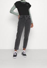 Svart kortärmad topp över en mintgrön polotröja, tillsammans med grå högmidjade jeans och svart-vita sneakers.