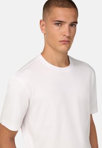 Balts kokvilnas T-krekls ar apaļu kakla izgriezumu un īsām piedurknēm, ar gludu tekstūru un brīvu fit. Nav redzamu rakstu vai akcentu.