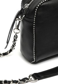 Sac à main en simili cuir noir avec des accents cloutés, matériel en argent, et une bandoulière en chaîne détachable. Présente une fermeture à glissière et une surface texturée.