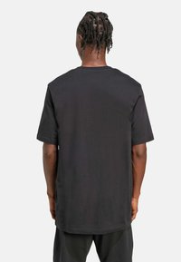 Crna kratka majica s kratkim rukavima, izrađena od mekog pamuka, s okruglim izrezom i slobodnim krojem te ravnim rubom.