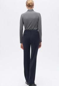 Grå långärmad topp med hög krage, kombinerad med marinblå vida byxor med två bakfickor och en mjuk, slät tyg.