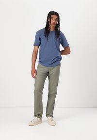 Blue short-sleeve henley shirt with three buttons, paired with light green pants and white sneakers. Simple and relaxed fit design.