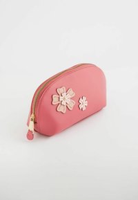 Neceser rosa hecho de material suave, con dos aplicaciones de flores color crema adornadas con detalles dorados y un cierre de cremallera.