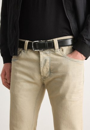 Jeans in denim beige con una texture sottile e cuciture blu chiaro, abbinati a una cintura in pelle nera con fibbia in argento.