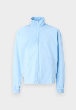 Light blue jacket with a high collar, full zip closure, and elastic cuffs. Features two front pockets and minimal branding on the chest.