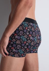 Boxers noirs avec un motif de récif corallien multicolore. Dotés d'une taille élastique noire et d'un ajustement serré. Texture de tissu douce et lisse.