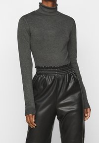 Szary sweter z golfem wykonany z prążkowanej tkaniny, z długimi rękawami, w połączeniu z czarnymi skórzanymi spodniami o wysokim stanie, z elastycznym pasem.