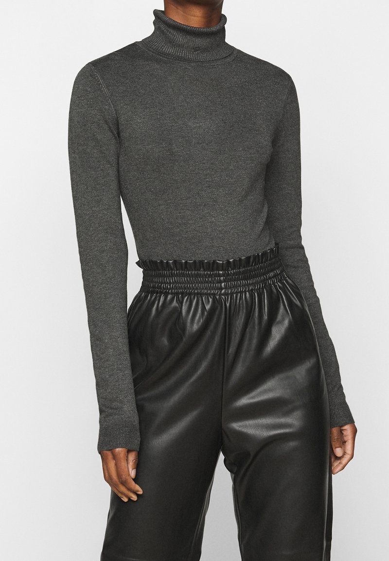 Szary sweter z golfem wykonany z prążkowanej tkaniny, z długimi rękawami, w połączeniu z czarnymi skórzanymi spodniami o wysokim stanie, z elastycznym pasem.