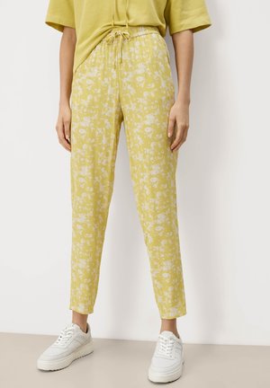 Pantalons floraux jaune clair avec une taille élastique et un cordon de serrage. Le tissu a une texture subtile et se porte avec des baskets blanches.