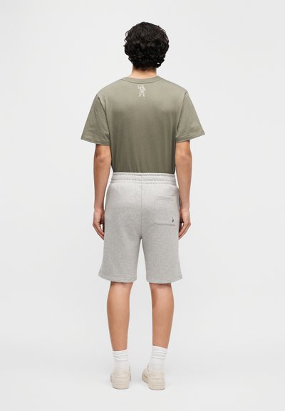 Φανέλα από βαμβάκι σε ελιά πράσινο χρώμα με γραφικό στο πίσω μέρος, συνδυασμένη με σορτς φούτερ σε ανοιχτό γκρι, μήκους μέχρι τη μέση της γάμπας, κατασκευασμένα από μαλακό, υφασμένο ύφασμα.