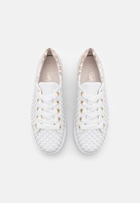 White woven sneakers featuring a textured surface and gold-tone eyelets. White laces and a light-colored interior complete the design.