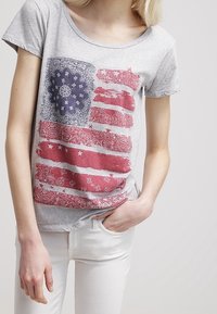 Gray cotton t-shirt featuring a distressed graphic print of the American flag in red, white, and blue with paisley accents.
