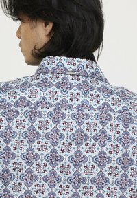 Weißes Hemd mit aufwendigem roten und blauen Blumenmuster; verfügt über einen strukturierten Kragen und ein kleines Markenetikett nahe dem hinteren Kragen.