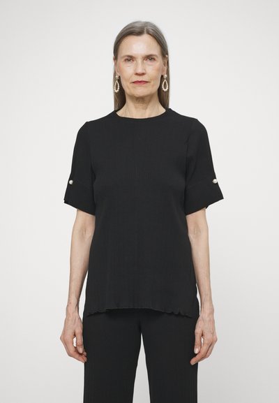 Black ribbed top with short sleeves, featuring pearl accents on sleeves and a scalloped hem. Soft fabric with a relaxed fit.