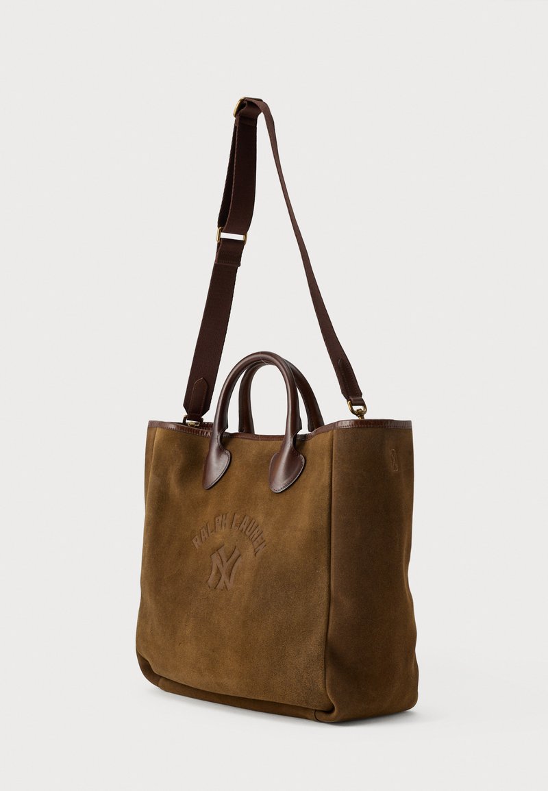 Brun ruskinds tote bag med læderdetaljer, top håndtag og justerbar rem. Har prægede logoer på forsiden og en struktureret form.