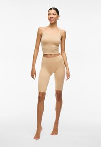 Top corto beige ajustado con tirantes finos, combinado con pantalones cortos a mitad del muslo del mismo color, ambos hechos de una tela suave y elástica. Diseño simple, bordes sin costuras.