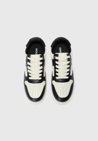 Zwarte en crèmekleurige sneakers met geperforeerde neus, zwarte veters en logo op de tong. Geweven materiaal en ronde vorm.