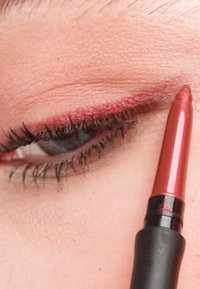 Rød øjenblyant påført langs den øverste øjenlågskant. Spidsen er spids med en glansfuld finish. Vipperne er mørke og krøllede med en diskret pink baggrund.