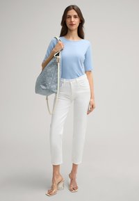 Helles blaugraues Kurzarmoberteil, weiße gerade Hosen, transparente Absatzsandalen und eine gemusterte blaue Einkaufstasche mit weißen Akzenten.