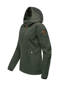 Veste à capuche vert foncé avec fermeture éclair frontale et poche latérale zippée, ornée d'un patch rond en cuir sur la partie supérieure de la manche gauche.