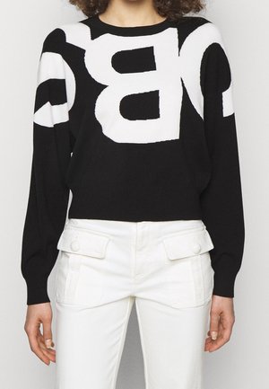 Sort-hvid sweater med store, markante bogstaver kombineret med hvide, højtaljede bukser med store lommer med knaplåse.