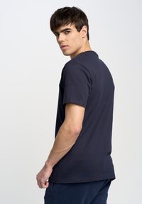 Camiseta de algodón azul marino con mangas cortas y cuello redondo, con un diseño liso. La tela parece suave y lisa, adecuada para el uso casual.