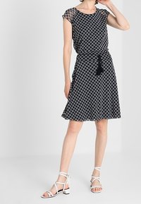 Vestido de estampado en blanco y negro con mangas cortas, cintura ajustada y falda acampanada; combinado con sandalias de tacón blanco y cintas.