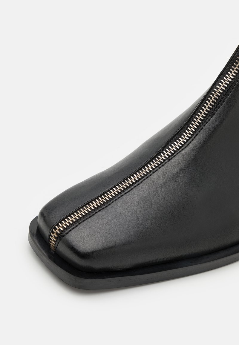 Schwarze Leder-Stiefeletten mit spitzem Zehenbereich, seitlichem Reißverschluss und glatter Textur. Verfügt über eine flache Gummisohle und minimalistische Nahtdetails.
