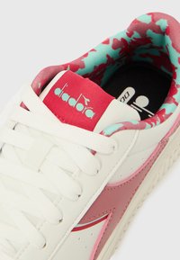 Λευκό δερ μάτινο αθλητικό παπούτσι με ροζ λεπτομέρειες και κορδόνια ως κλείσιμο. Το εσωτερικό διαθέτει τουρκουάζ και ροζ μοτίβο παραλλαγής. Η μάρκα εμφανίζεται στη γλώσσα.