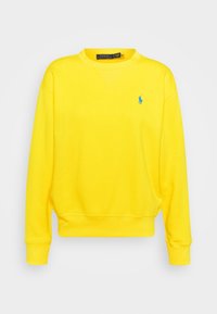 Gul sweatshirt i mjuk bomull med rund halsringning, ribbad mudd och en liten blå polo-logotyp på bröstet. Slät textur.