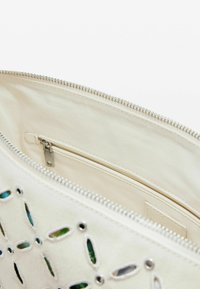 Interno di una borsa in tessuto beige con una tasca con zip. Presenta ritagli decorativi e dettagli metallici lungo la cerniera per un tocco in più.