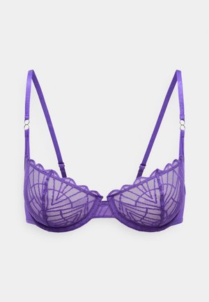 Lilla pitsbra, millel on geomeetriline muster, sakilised servad ja reguleeritavad rihmad. Omab siledat tekstuuri ja metallist rõngaste aksessuaare.