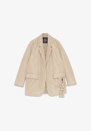 Beige gepolsterte Blazer mit Reverskragen, zwei vorderen Taschen, Knopfverschluss und einem abnehmbaren Plüsch-Anhänger an der Seite. Glatte Textur.