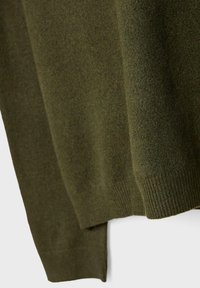 Primo piano di un tessuto lavorato a maglia verde oliva che mostra i polsini testurizzati delle maniche e le pieghe morbide del materiale.