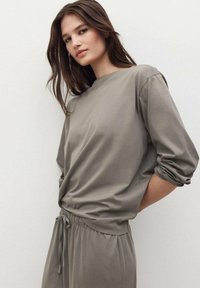 Top de corte holgado, de manga larga y cuello redondo, en suave tela gris apagado, con mangas con puños y una cintura ligeramente fruncida.