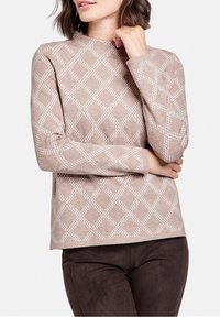 Top a maniche lunghe color beige chiaro con motivo a rombi texture bianchi, caratterizzato da un collo alto e maniche aderenti. Abbinato a pantaloni marroni.