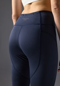 Navy high-waisted leggings made of stretchy fabric with flatlock seams, featuring a logo at the back and a contouring fit.
