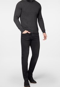 Mörkgrå tröja med rund halsringning, åtsittande ärmar och ribbade muddningar, parat med svarta, slim-fit jeans och mörka stövlar.