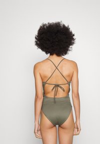 Olivengrønn one-piece badedrakt med ribbet tekstur, kryssede stropper bak og en knyttet detalj bak, som har et utskjæringsdesign.