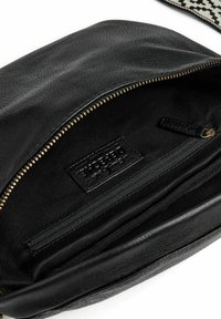 Interno di una borsa in pelle nera con una tasca con zip e etichetta del marchio. Texture liscia, zip dorata e foderata in tessuto nero.