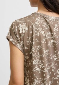 Brun blomsterbluse med et glat stof, korte opsm�øgede ærmer og et diskret hvidt blomstermønster over hele stoffet.
