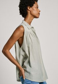 Camicia senza maniche verde chiaro con colletto, design plissettato, texture morbida e vestibilità ampia, con fessure ai fori delle braccia.