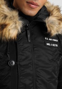 Black padded jacket featuring a faux fur hood, front zip closure, buttons, and "U.S. AIR FORCE" embroidered patch details.
