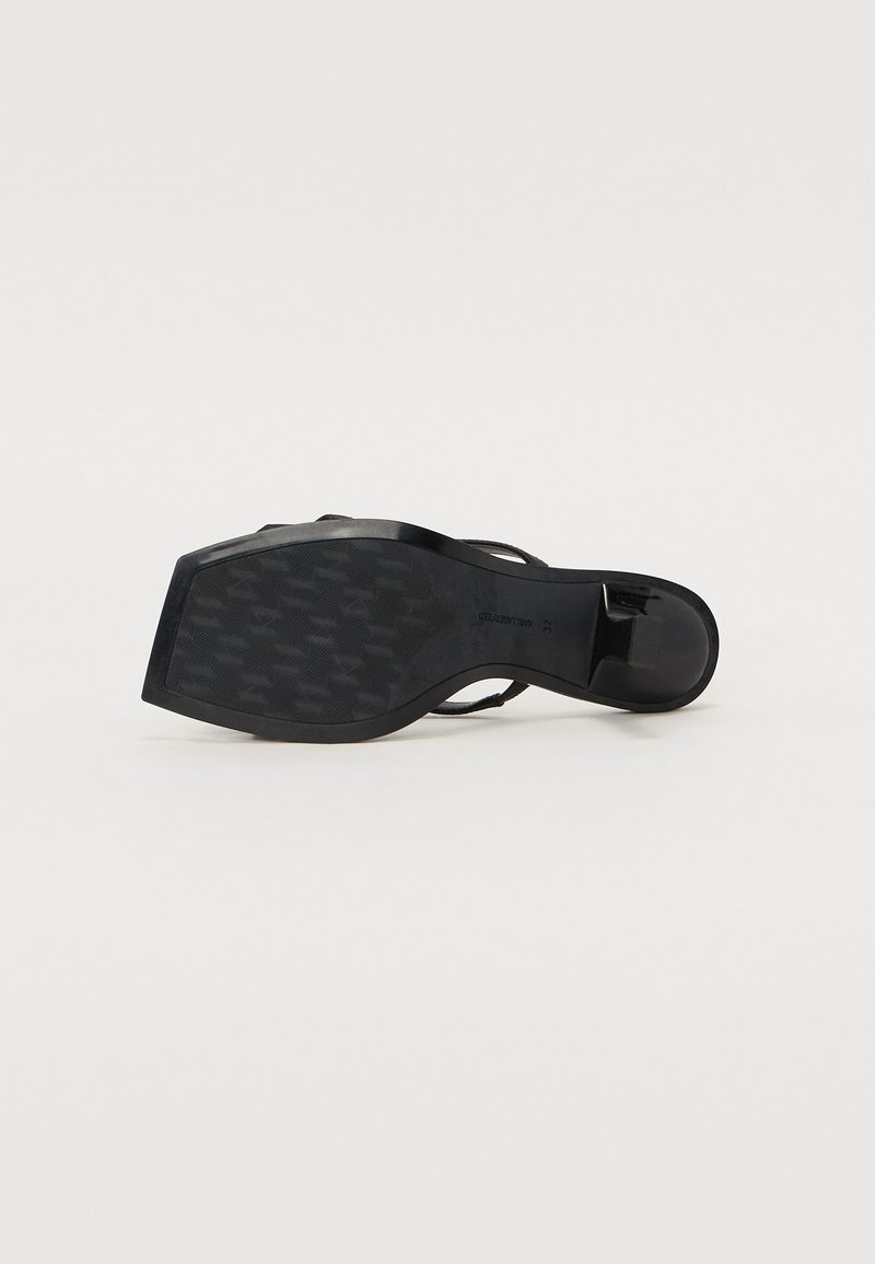 Schwarze hochhackige Sandale mit geschlossenem Rücken, schlanken Riemen und einer strukturierten Gummisohle mit einem Hahnentrittmuster.