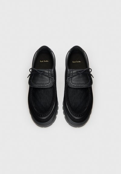 Black shoes made of textured leather with a smooth toe cap, featuring a woven accent, lace-up design, and thick rubber soles.