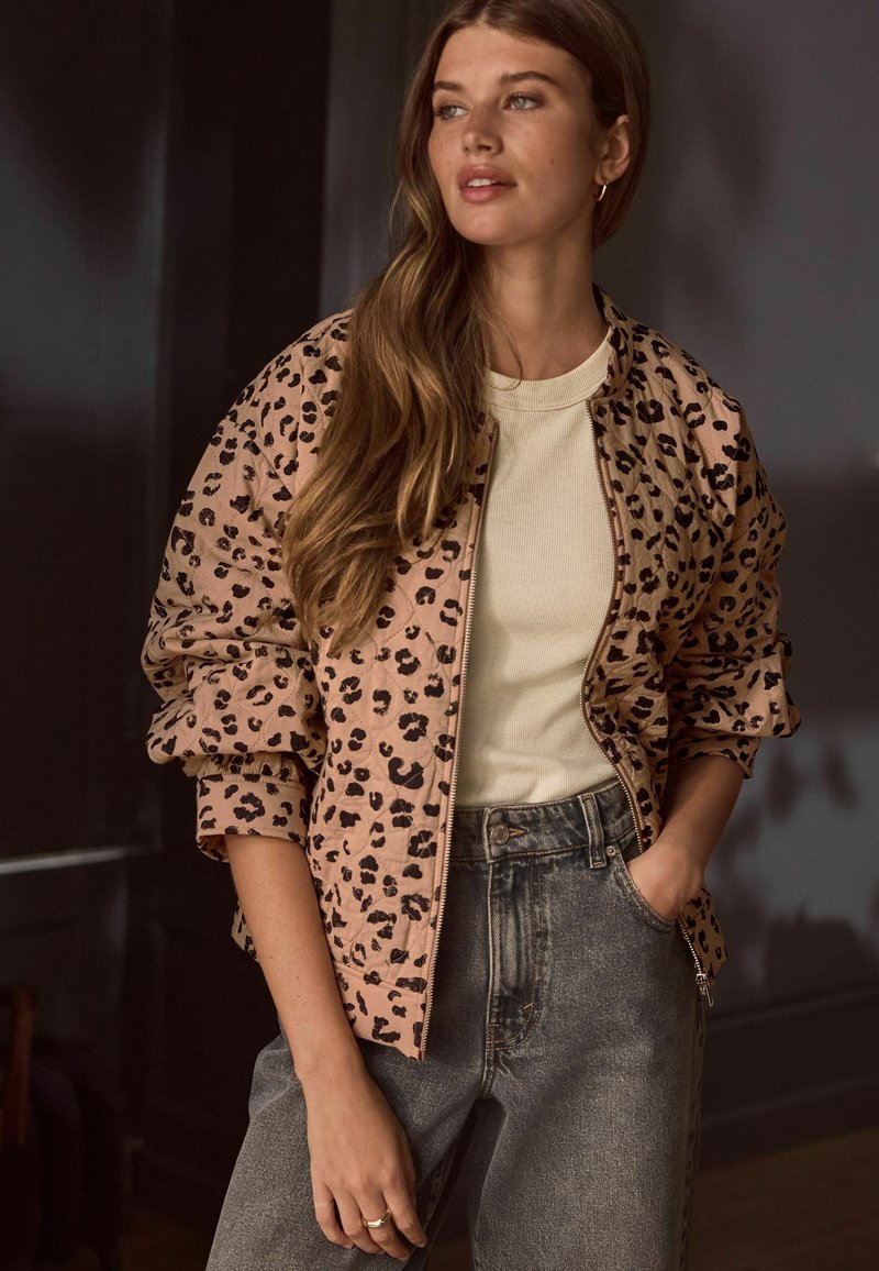 Leopardmønstret bomberjakke i lys beige, med ribbede manchetter og lynlås. Båret over en cremefarvet tætsiddende top og parret med højtaljede jeans.
