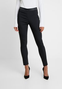 Schwarze Leggings aus einem glatten, dehnbaren Stoff, mit einem matten Körper und glänzendem Bündchen, eng anliegendem Design und knöchellanger Schnitt.